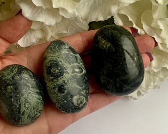 May include: Three green and black polished stones with swirling patterns. The stones are smooth and oval shaped.