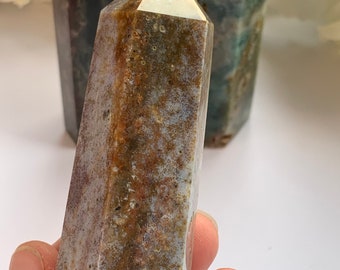 May include: A brown, green, and white agate crystal point. The crystal is polished and has a smooth, glassy surface. The point is about 4 inches tall.