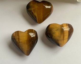 Puede incluir: Tres piedras de ojo de tigre en forma de corazón. Las piedras son de color marrón oscuro con rayas doradas y negras.