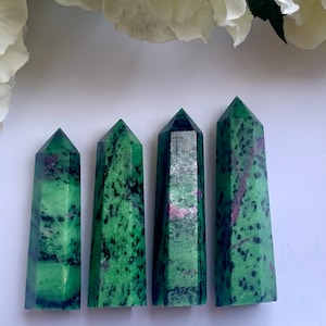 May include: Four green, black, and pink gemstone points, also known as green zoisite, are arranged in a row on a white surface.