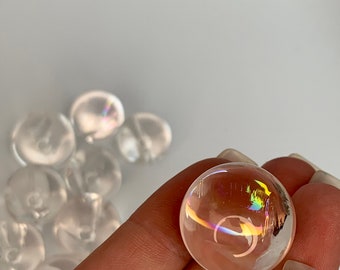 May include: A clear quartz crystal sphere with iridescent rainbow colours. The sphere is being held in a hand.