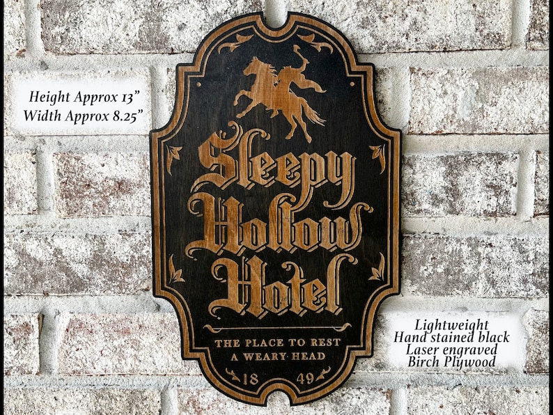 May include: A black and brown wooden sign with the words "Sleepy Hollow Hotel" in a decorative font. The sign is approximately 13 inches tall and 8.25 inches wide. It features a laser engraved image of a rider on horseback and the text "The place to rest a weary head". The sign is made of lightweight birch plywood and hand-stained black.