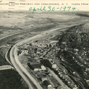 May include: An aerial view of a highway and river running through a town. The image was taken on April 30, 1974. The text "MOHAWK RIVER THRUWAY AND CANAJOHARIE, N.Y. TAKEN FROM AIR" is visible at the top of the image.