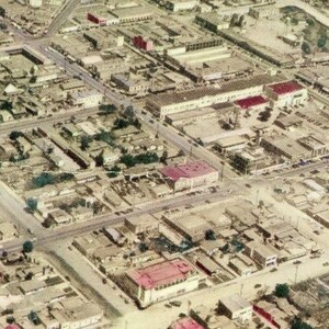 Puede incluir: Vista aérea de una ciudad con un trazado de calles en forma de cuadrícula. Los edificios de varios tamaños y formas están densamente agrupados. La imagen tiene un aspecto vintage, ligeramente descolorido, con colores apagados y una sensación de historia.