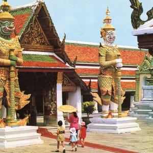 May include: Two large, colorful, ornate statues of mythical figures stand in front of a traditional Thai temple. The statues are made of wood and painted in bright colors. The temple is decorated with intricate carvings and colorful paint.