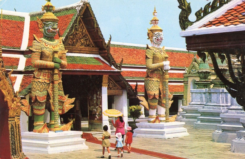 May include: Two large, colorful, ornate statues of mythical figures stand in front of a traditional Thai temple. The statues are made of wood and painted in bright colors. The temple is decorated with intricate carvings and colorful paint.