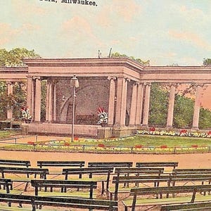 May include: Vintage postcard image of a classical outdoor performance venue with a stage, columns, and rows of benches. The venue is surrounded by greenery and flower beds, with a soft, faded color palette.