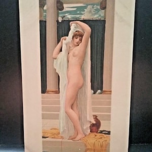 May include: A vintage postcard featuring a classical painting of a nude woman draped in a sheer white cloth. The artwork depicts a woman standing near a stone structure with columns, a terracotta vase, and draped yellow fabric.
