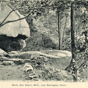 May include: A black and white photograph of a rocky outcropping in a wooded area. The rock formation is labeled "Bluffs" and the caption reads "Wolfs Den Dean's Mills, near Stonington, Conn."