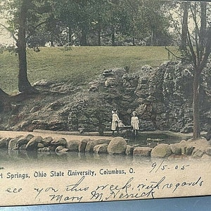 Puede incluir: Una postal en blanco y negro que muestra un paisaje rocoso con un pequeño estanque y dos figuras de pie cerca del agua. La postal está fechada el 9/5-05 y tiene el texto "Siebert Springs, Ohio State University, Columbus, O." y un mensaje escrito a mano que dice "Sending to you this week, with regards Mary M. Nernick".