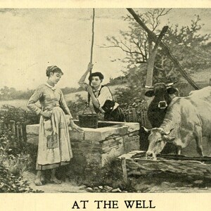 以下が含まれることがあります： 「AT THE WELL」と題されたセピア色のヴィンテージポストカード。石造りの井戸にいる2人と、近くにいる牛が描かれています。1人がバケツで水を汲んでいます。シーンは田園風景の中に設定されています。