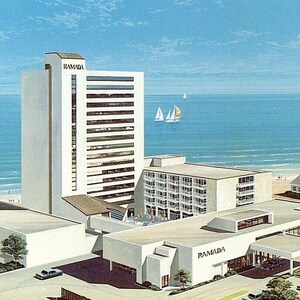 May include: An illustration of a Ramada hotel complex on a beach. The hotel features a tall, white tower and several low-rise buildings. The sea is in the background with sailboats.