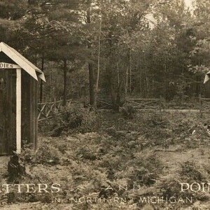 May include: Vintage black and white photograph of two outhouses in a wooded area. One is labeled "Ladies" and the other "Gents". The text at the bottom reads "Setters and Pointers in Northern Michigan."