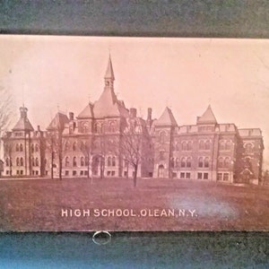 Op de afbeelding: Een zwart-witte vintage ansichtkaart met een groot bakstenen gebouw met een hoge centrale toren. Het gebouw is gelabeld "HIGH SCHOOL,OLEAN, N.Y."