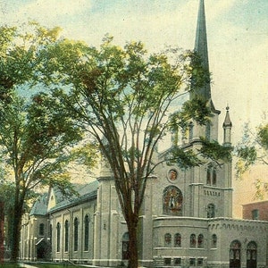 Könnte beinhalten: Eine alte Postkarte, die eine große, graue Steinkirche mit einem hohen, spitzen Turm zeigt. Die Kirche hat ein großes Buntglasfenster und ist von Bäumen umgeben.
