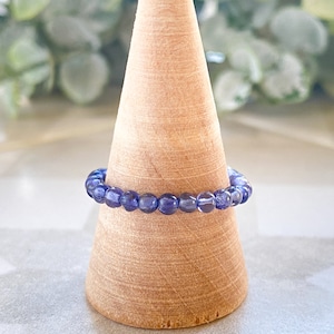 May include: A purple gemstone beaded ring on a wooden ring display stand.