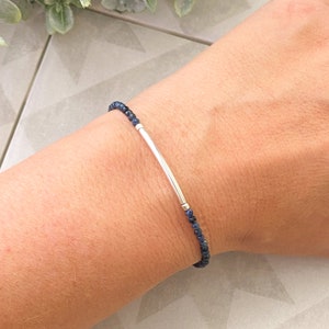 May include: A delicate bracelet featuring a silver bar and small blue gemstone beads.