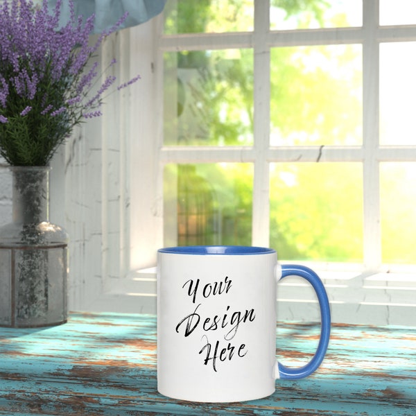 Mockup of 11oz white mug with blue accent color in a rustic lifestyle setting with lilacs in front of a window with the sunrise