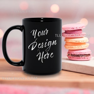 Mockup of 15oz black mug  in a cozy lifestyle setting with macarons and a book on a counter