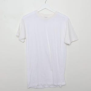 May include: A plain white t-shirt hangs from a white hanger against a white backdrop. The short-sleeved shirt has a crew neck and appears to be made of a soft, lightweight fabric. The shirt is a basic, versatile garment.