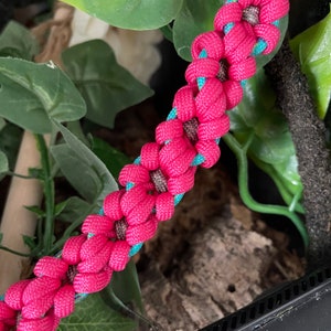 May include: A pink and teal paracord bracelet with a woven flower pattern.