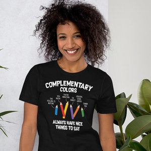 Puede incluir: Camiseta negra con un gráfico blanco de lápices de colores y el texto "Colores complementarios" y "Siempre ten cosas agradables que decir".