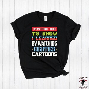 Puede incluir: Camiseta negra con un gr&aacute;fico colorido que dice "Todo lo que necesito saber lo aprend&iacute; viendo *los ochenta* dibujos animados".