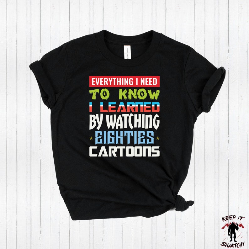 Puede incluir: Camiseta negra con un gr&aacute;fico colorido que dice "Todo lo que necesito saber lo aprend&iacute; viendo *los ochenta* dibujos animados".