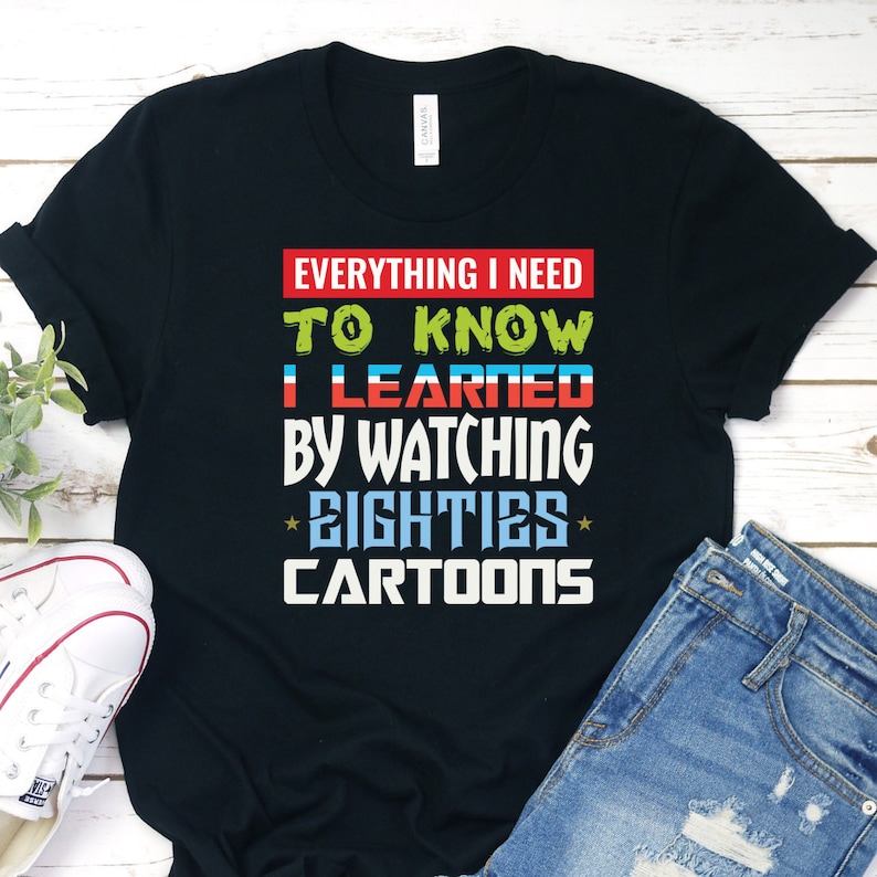 Puede incluir: Camiseta negra con el texto "Todo lo que necesito saber lo aprend&iacute; viendo dibujos animados de los ochenta" en letras de colores.