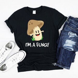 Könnte beinhalten: Schwarzes T-Shirt mit einem Cartoon-Pilz-Motiv und dem Text "I'm a Fungi!"
