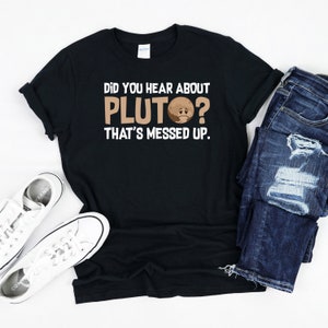 May include: Black t-shirt with white text that reads "Did you hear about Pluto? That's messed up." A cartoon image of Pluto with a sad face is included in the text.