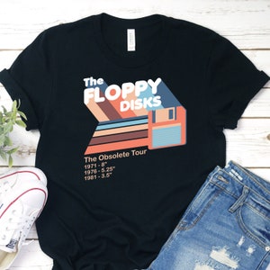 以下が含まれることがあります： フロッピーディスクと「The Floppy Disks The Obsolete Tour 1971 - 8" 1976 - 5.25" 1981 - 3.5」というテキストがレトロなスタイルで描かれた黒いTシャツ