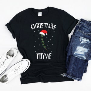 May include: Black t-shirt with a white graphic of a sprig of thyme wearing a Santa hat. The text "Christmas Thyme" is printed below the graphic.