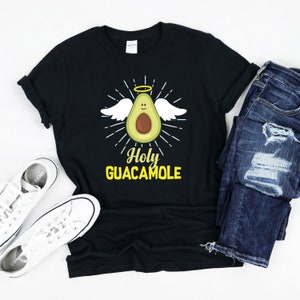Puede incluir: Camiseta negra con un aguacate de dibujos animados con un halo y alas. El texto "Holy Guacamole" está impreso en amarillo debajo del aguacate.