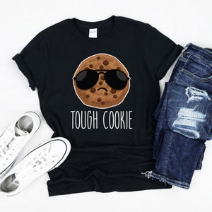 May include: A black t-shirt with a brown chocolate chip cookie wearing sunglasses and the text "TOUGH COOKIE" in white.