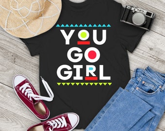 May include: Black t-shirt with a white graphic that says "YOU GO GIRL" in a retro style with colorful accents.