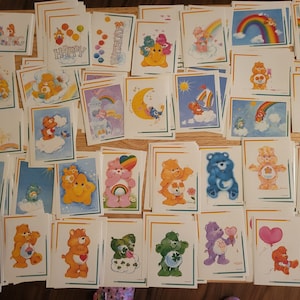 May include: A collection of 30 Care Bear stickers featuring various Care Bears with different expressions and poses. The stickers are on a white background with a rainbow border.