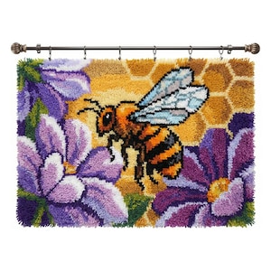 May include: A colorful, textured wall hanging featuring a bee with orange and black stripes, light blue wings, and a honeycomb background. The bee is surrounded by purple flowers. The wall hanging is attached to a brown metal rod.