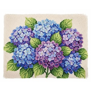 Op de afbeelding: Een rechthoekig tapijt met een bloemenontwerp van blauwe en paarse hortensia's en groene bladeren. De bloemen zijn dicht opeengepakt, waardoor een textuur ontstaat tegen een beige achtergrond. Het tapijt heeft een gefranjerde rand.