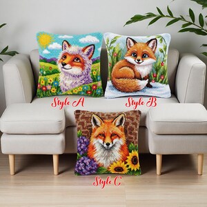 Op de afbeelding: Drie decoratieve kussens met vossenontwerpen. Stijl A toont een vos in een landschap met een zon. Stijl B toont een vos in een besneeuwde scène. Stijl C heeft een vos met zonnebloemen en paarse bloemen. Elk kussen heeft de stijlnaam erop gedrukt.