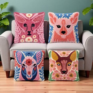 Op de afbeelding: Vier decoratieve kussens met dierengezichten. Elk kussen heeft een ander kleurenschema, waaronder roze, blauw en groen, met bloemen- en bladerpatronen. De kussens zijn vierkant en geplaatst op een grijze bank.