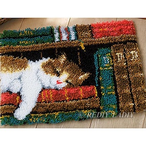 Pode incluir: Um gato branco com manchas marrons e laranja está enroscado em uma estante cheia de livros coloridos. O gato está dormindo e tem a cabeça apoiada em um livro vermelho. A estante é de madeira e tem um acabamento marrom.
