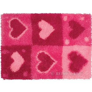 May include: A pink and red rug with a patchwork design of hearts. The rug is made of a soft, fluffy material.