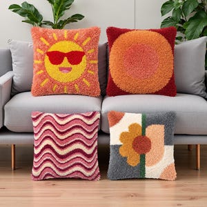 Peut inclure: Quatre coussins carrés avec une broderie texturée à l'aiguille. L'un présente un soleil jaune avec des lunettes de soleil rouges, un autre des cercles orange concentriques, un troisième des lignes ondulées roses et bordeaux, et un motif floral.