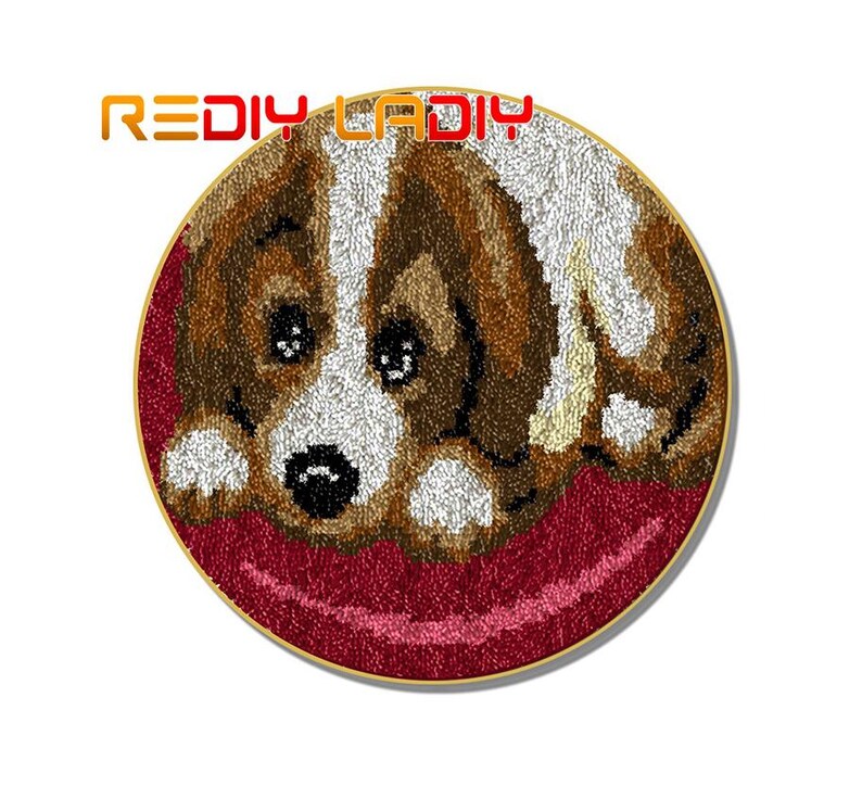 May include: A close-up of a brown and white dog with brown eyes, lying on a red background. The dog is made of yarn and is a rug hooking project.