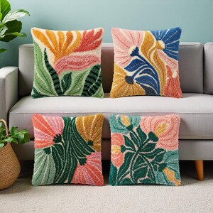 Peut inclure: Quatre coussins carrés avec des motifs floraux. Chaque coussin présente un motif floral coloré différent dans les tons orange, rose, bleu, jaune et vert. Les coussins sont placés sur un canapé gris.