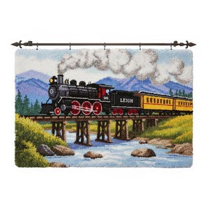 Puede incluir: Tapiz texturizado que representa un tren de vapor cruzando un puente de madera sobre un río. El tren es negro con ruedas rojas y un vagón amarillo. La palabra "LEIGH" es visible en el tren. El fondo presenta montañas y un cielo nublado.