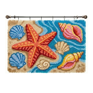Könnte beinhalten: Ein rechteckiger Wandbehang aus Knüpftechnik mit einem großen orangefarbenen Seestern, zwei blauen Jakobsmuscheln, einer rosa Flügelschnecke und einer gelben Spiralschnecke auf sandigem Grund und blauem Wasser, an einer dunklen Metallstange.