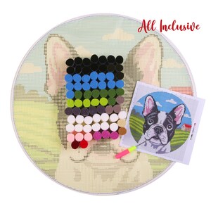 Op de afbeelding: Een ronde, gebroken witte canvas met een Franse Bulldog-ontwerp, met een kleurenpalet van zwart, blauw, groen en wit. De kit bevat een verscheidenheid aan kleurrijke garenbundels en een kleine gedrukte gids. De woorden "All Inclusive" zijn in het rood geschreven.