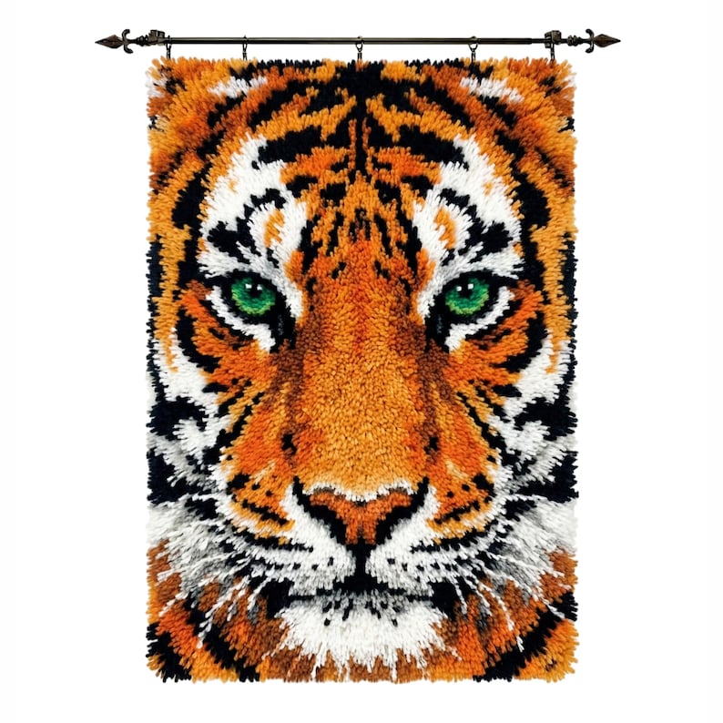 Op de afbeelding: Een wandkleed met een close-up van een tijgergezicht. De tijger heeft oranje vacht met zwarte strepen, witte accenten en opvallende groene ogen. Gemonteerd op een stang met decoratieve uiteinden.